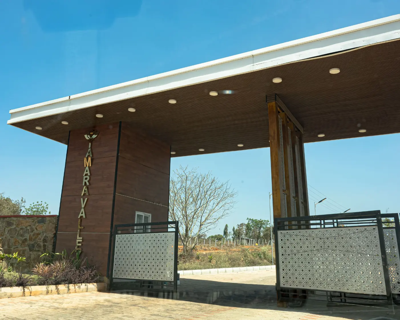 Side view of tamara valley’s modern entrance gate with open farmland beyond.